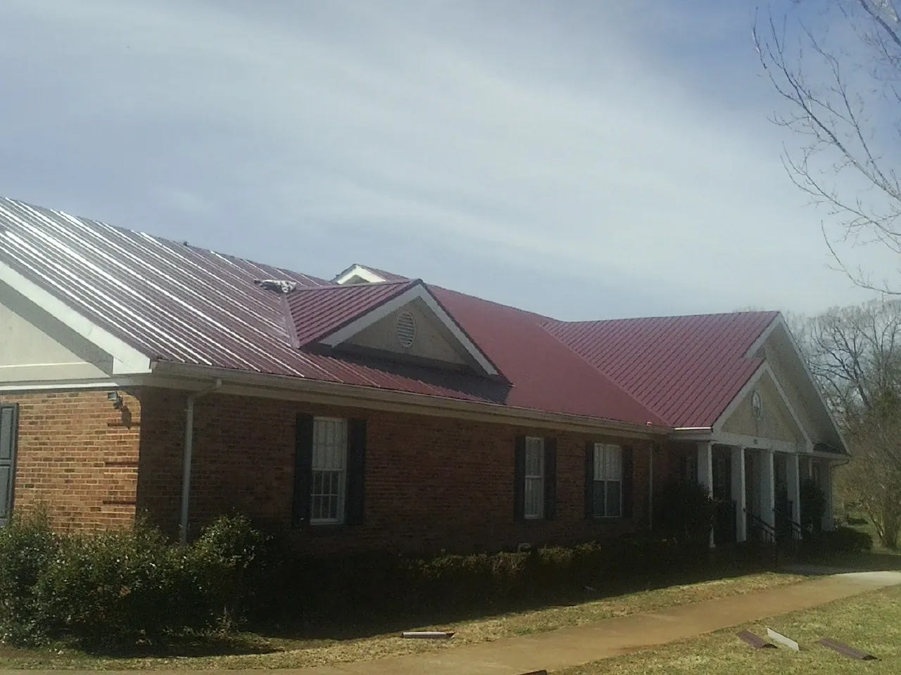 Red metal roof with gabled entries on a long brick building, from a Hail Damage Roof Repair job in Lowell