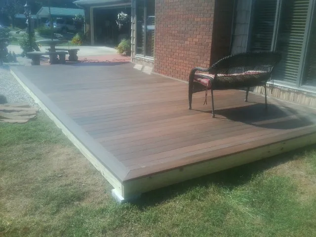 New wood deck and wicker chair beside a brick house in Lowell