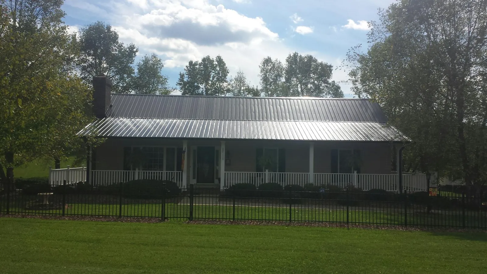 Gray metal roof on a brick ranch with a full width front porch — Gutter Guard Installation work by our crew in Lowell