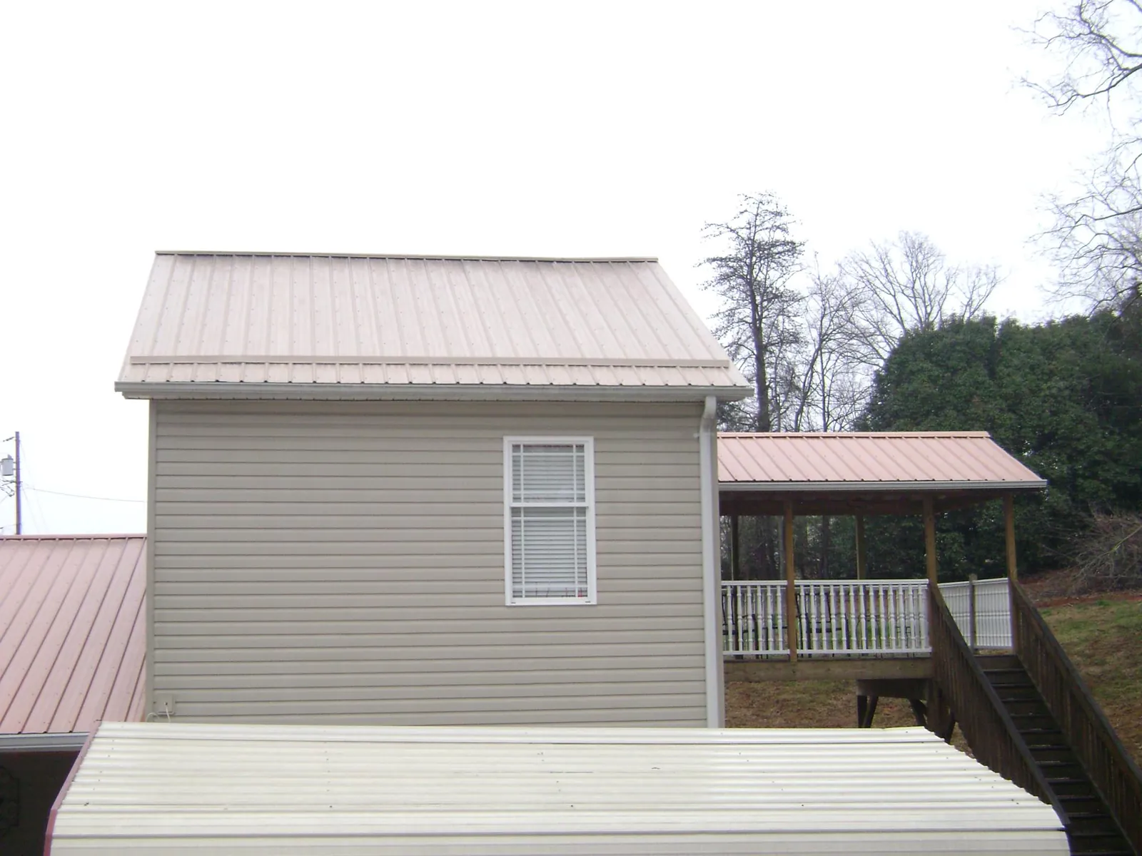 Tan metal roofs on a two story addition and attached porch, from a Roof Replacement job in Lowell